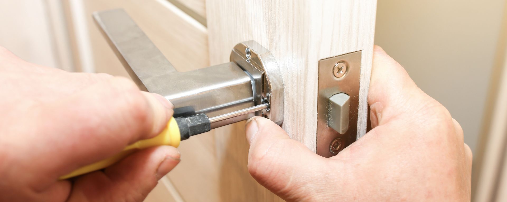 Mani che usano un cacciavite per installare una serratura argentata su una porta di legno.