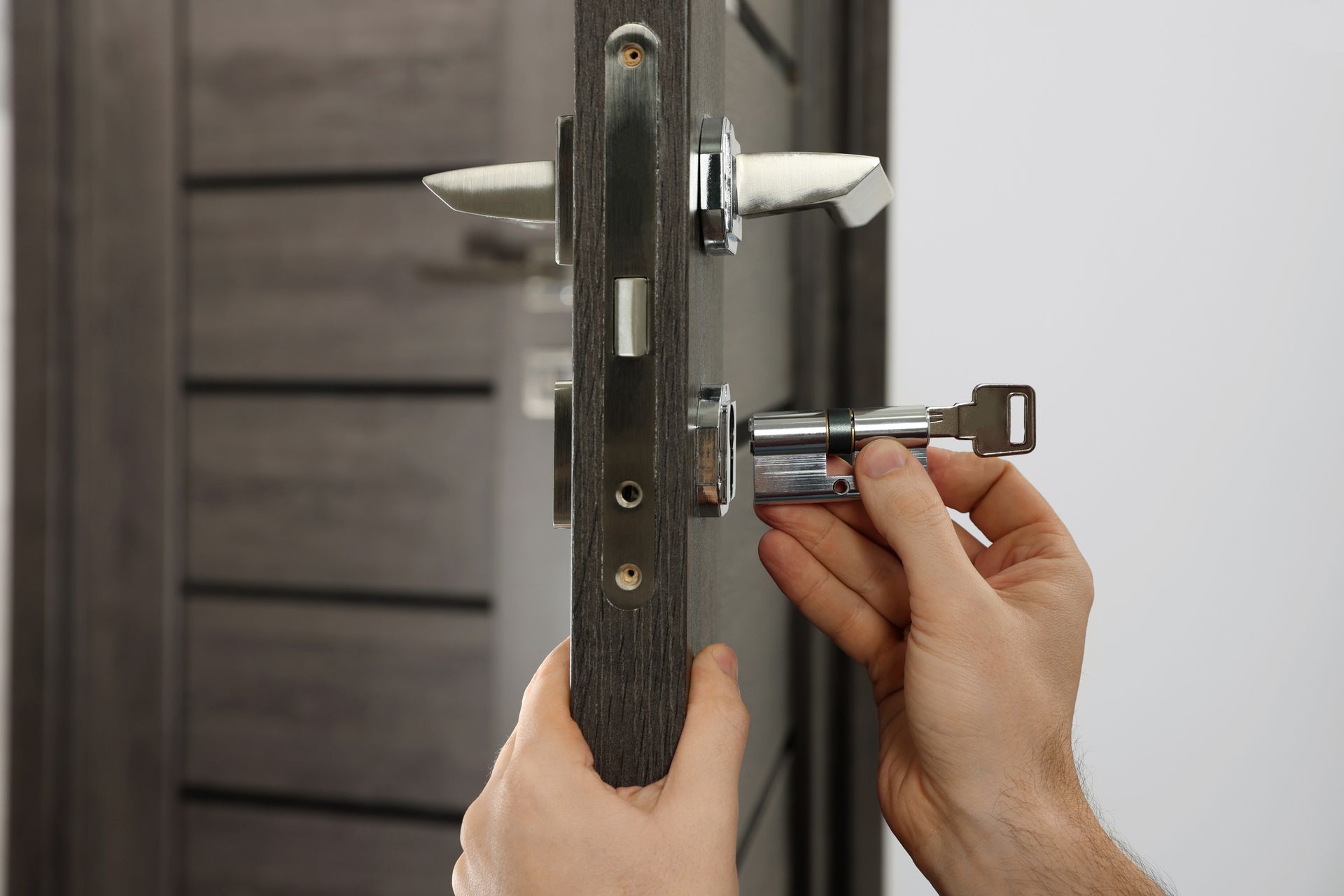 Mani che installano una serratura argentata su una porta di legno scuro con un cacciavite