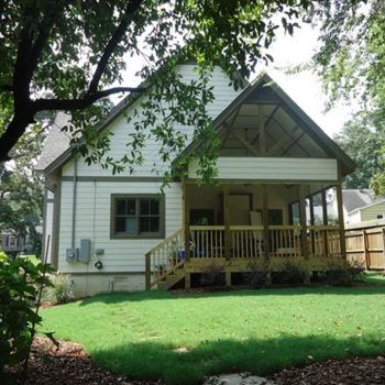 White house with wooden porch and green lawn.