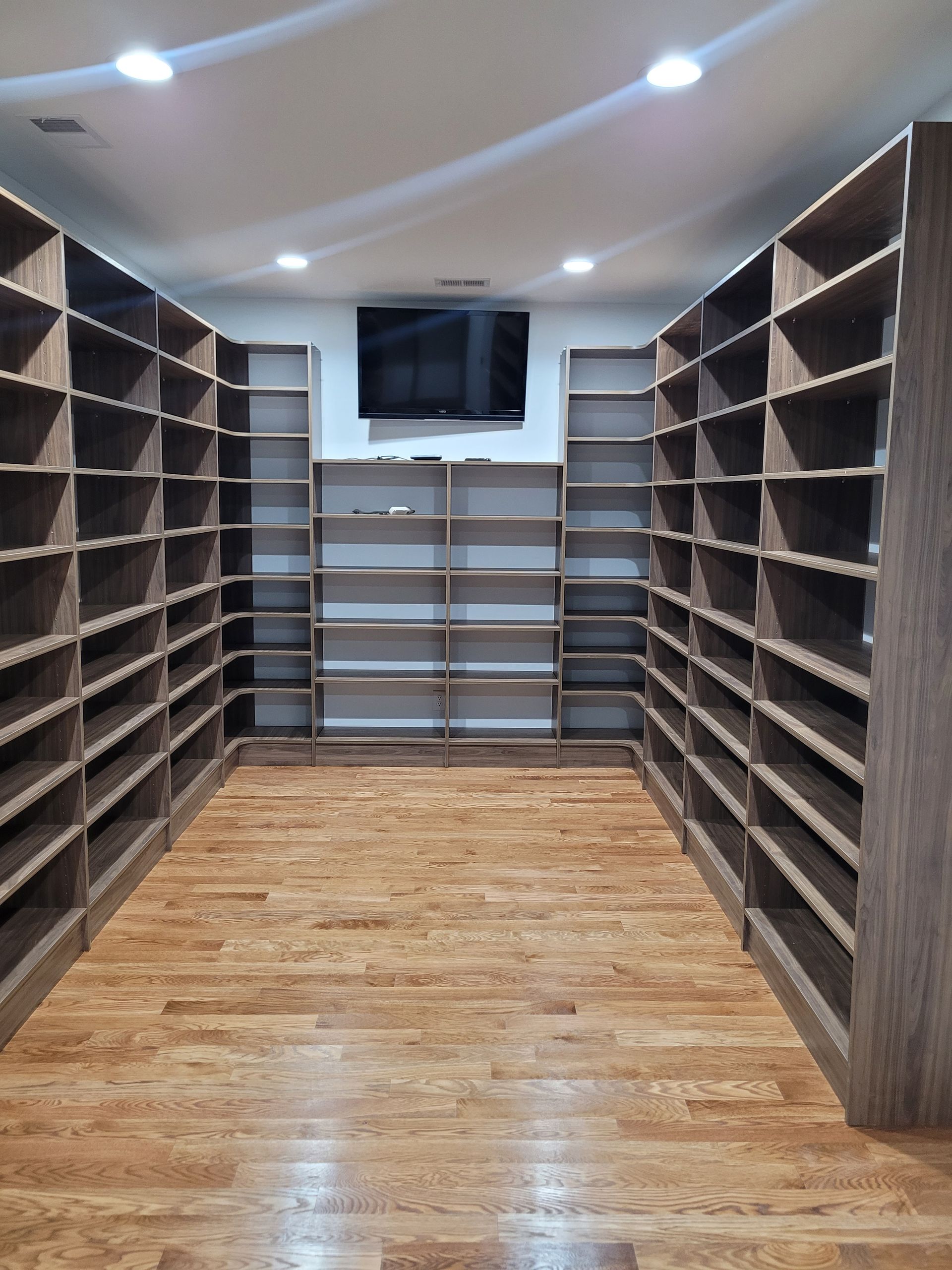 A room with built-in shelves on three walls, wood floor, and a TV above center shelves.