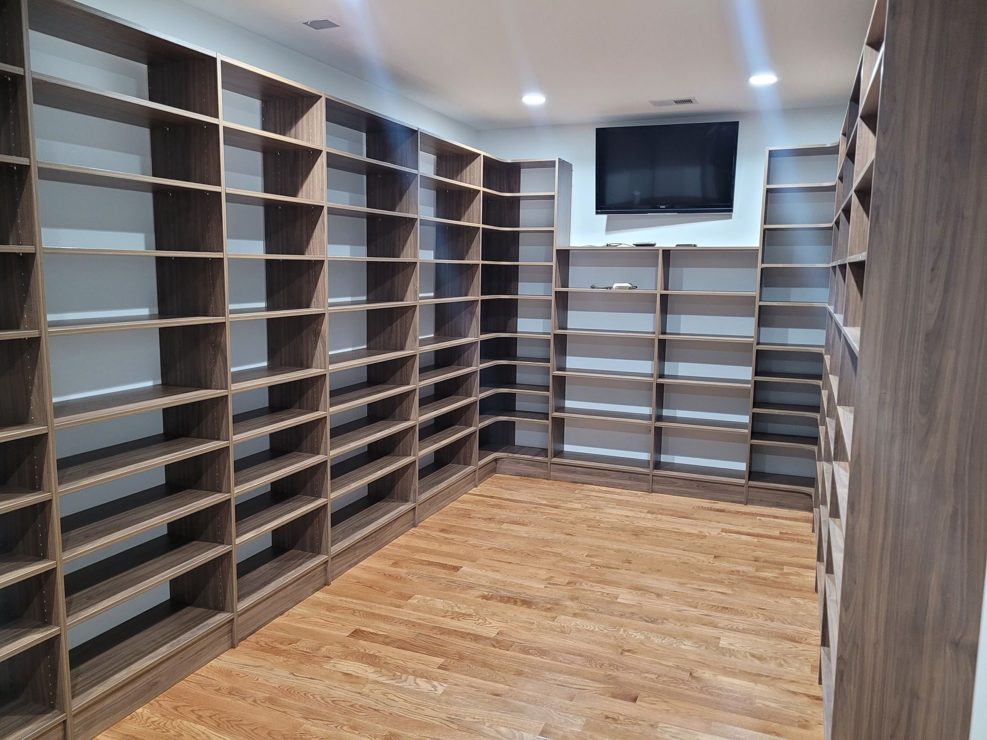 Empty wooden bookshelves line the walls of a room with a hardwood floor and TV.