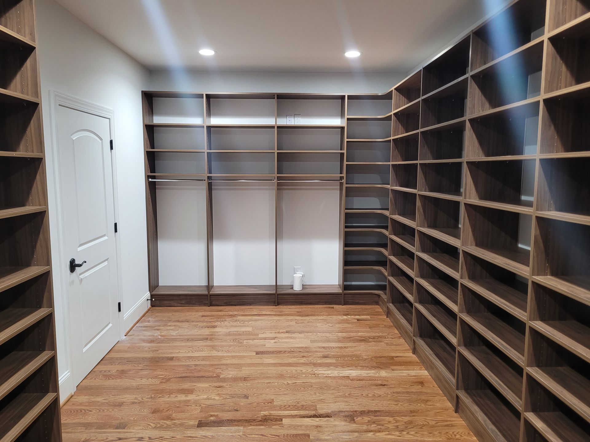 Empty walk-in closet with dark wood shelving, light wood floor, white door.