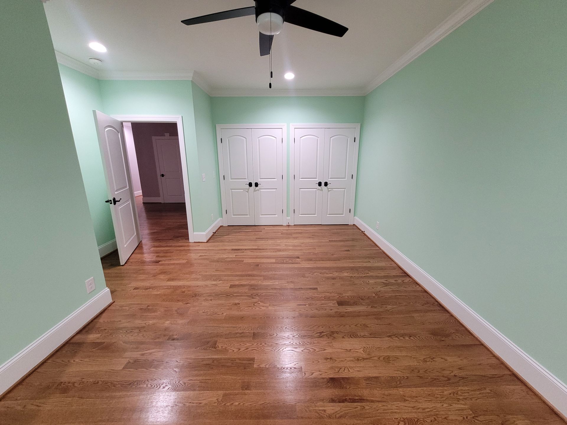 Empty bedroom with hardwood floors, mint green walls, white trim, and closet doors.