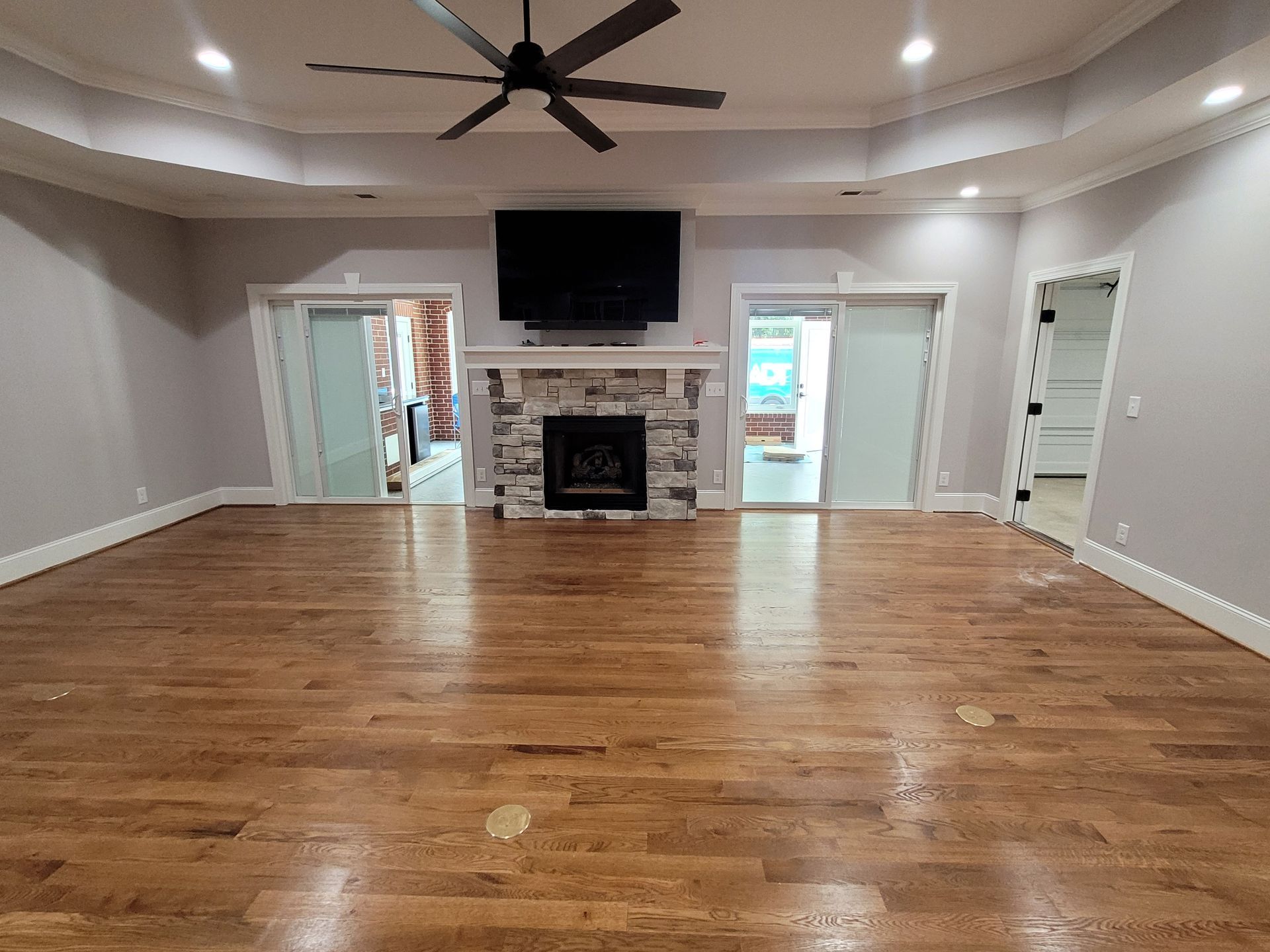 Spacious living room with hardwood floors, fireplace, mounted TV, and two sliding doors.