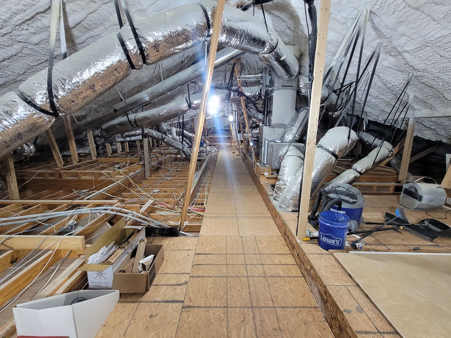 Attic with HVAC ductwork, wooden beams, and a pathway. Bright light at the end.