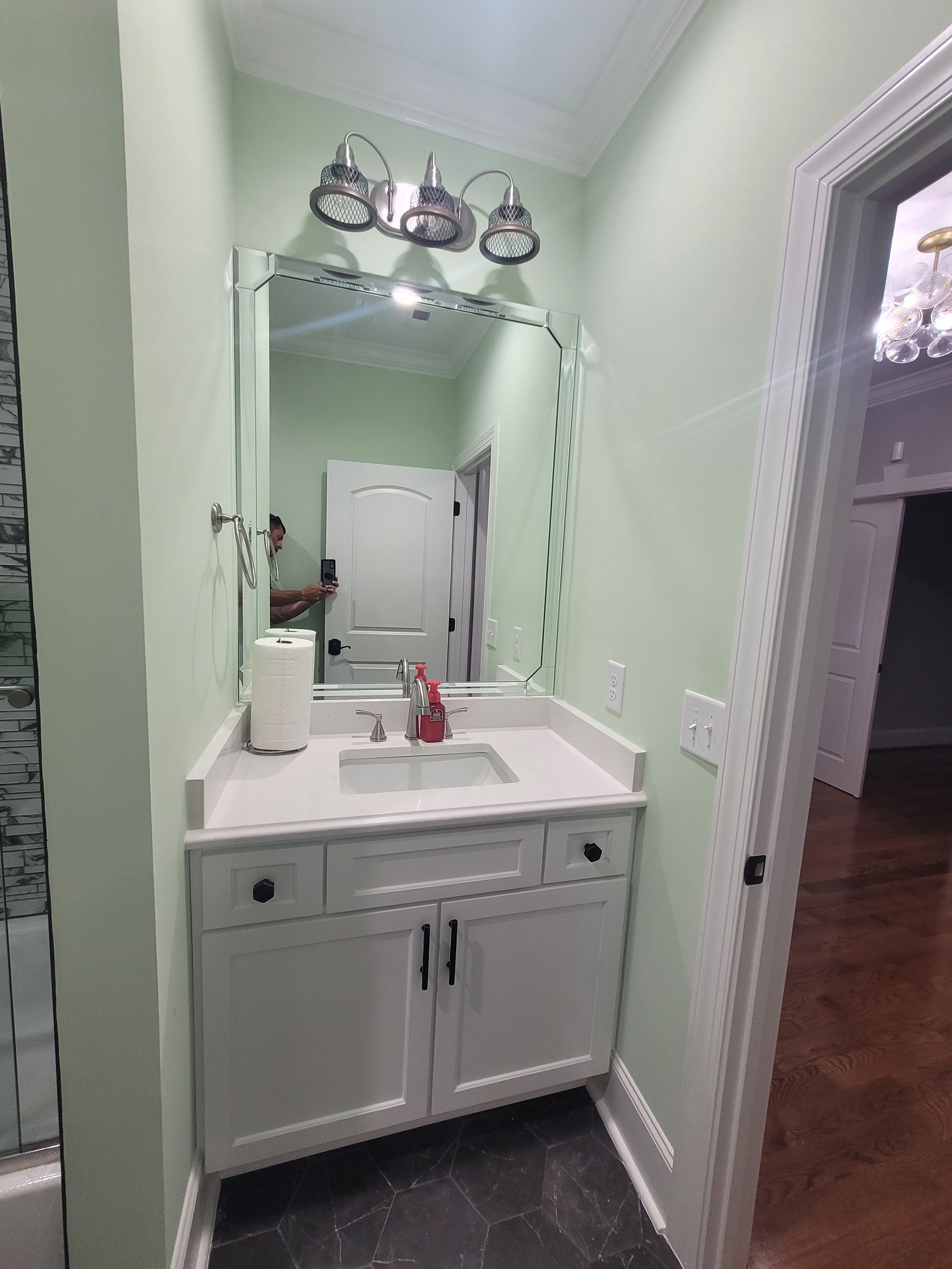 A small, white bathroom vanity with a matching mirror, light fixtures, and pale green walls.