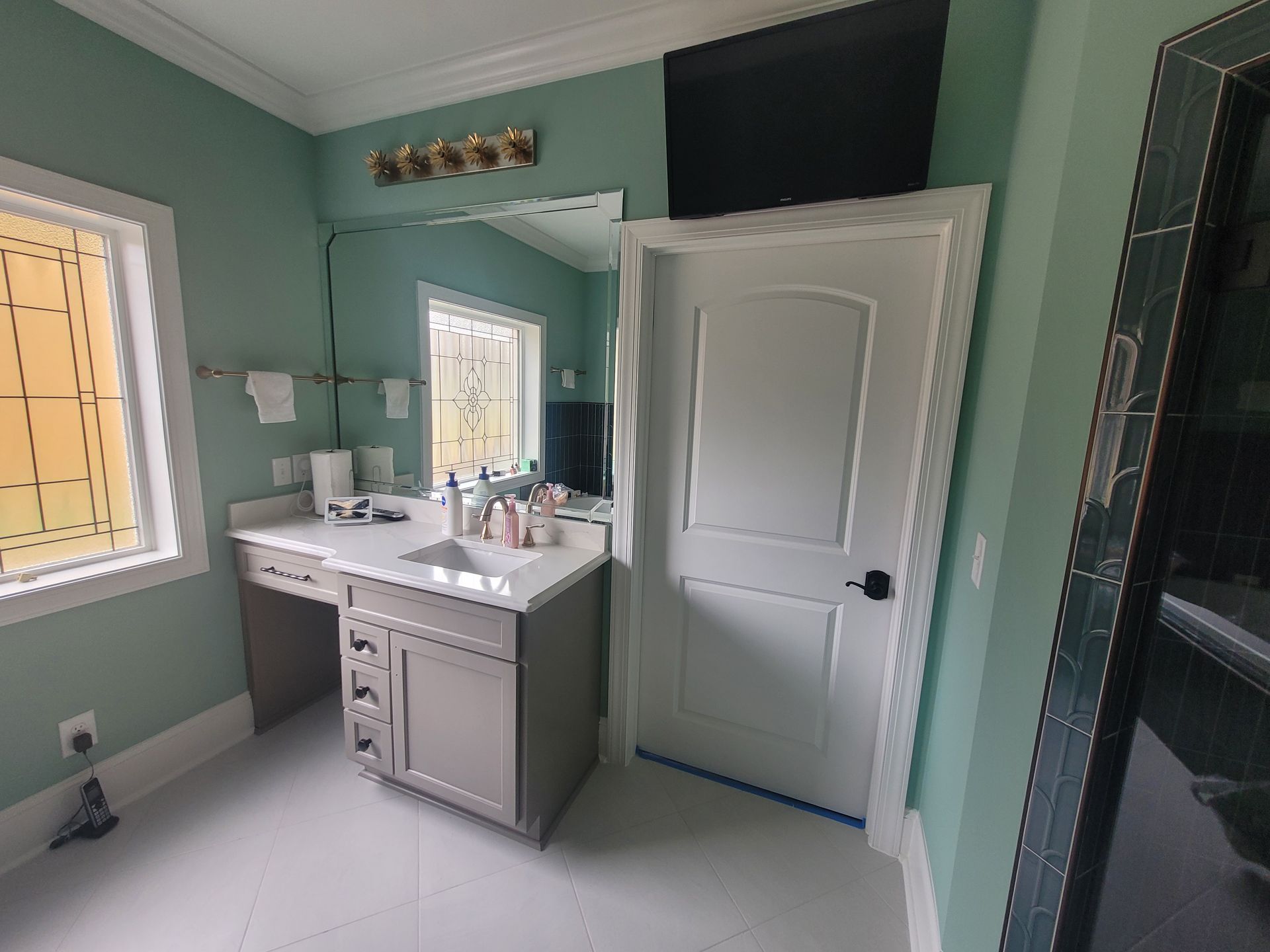 Bathroom with light blue walls, gray vanity, white door, window, and large mirror.