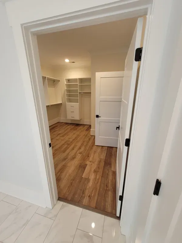 White-walled room doorway leading into a walk-in closet with shelves, a white door, and wood-look flooring.