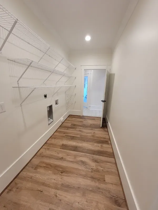 Laundry room with white walls, wire shelves, and wood-look flooring. Open door in the distance.