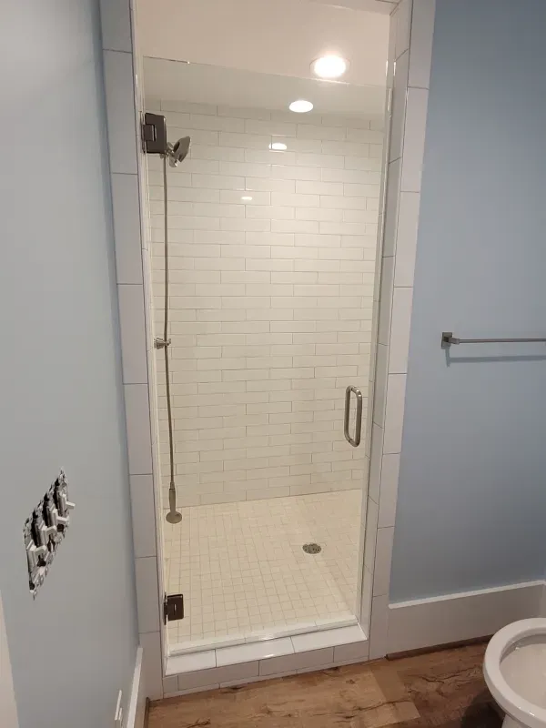 Shower with clear glass door and white tile interior, with light blue walls.