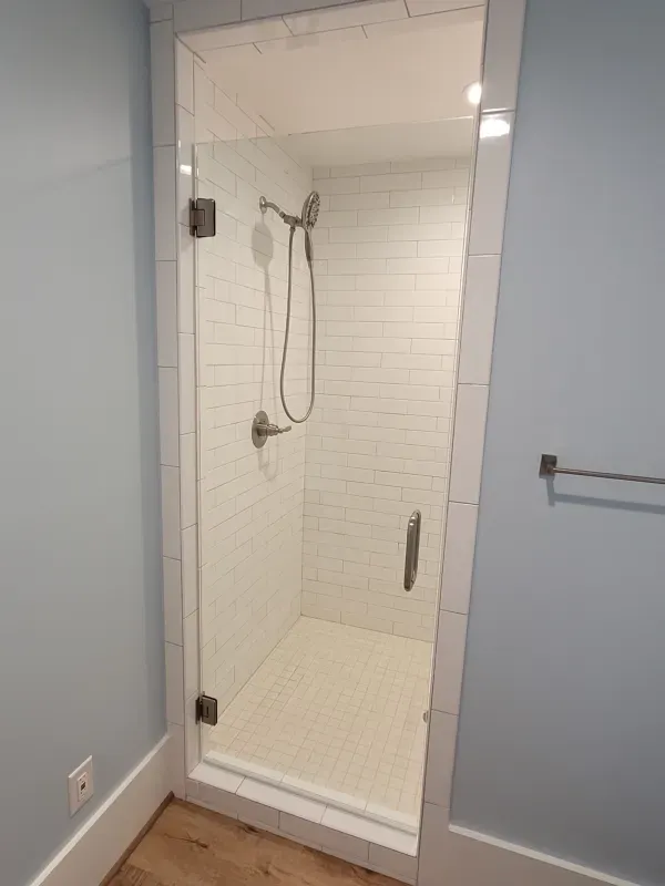Glass-doored shower with white tiled walls and floor. A silver showerhead hangs from the wall.