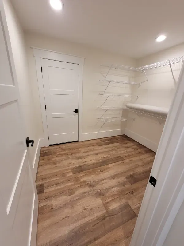 Walk-in closet with wood floors, white walls, shelving, and a closed white door.