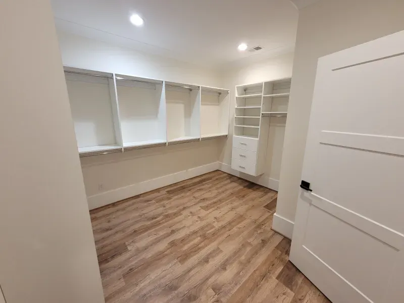 Empty walk-in closet with white shelving and wood-look flooring. A white door is ajar.