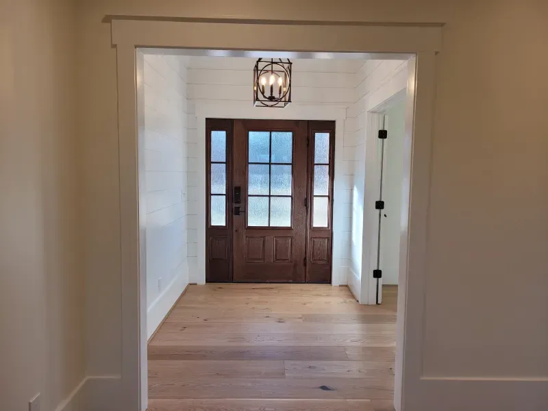 Wooden door with sidelights and transom, viewed from hallway. Light oak floors and white walls.