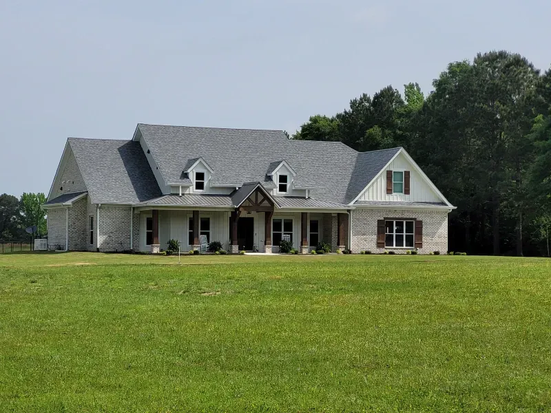 Large light brick house with gray roof and green yard.