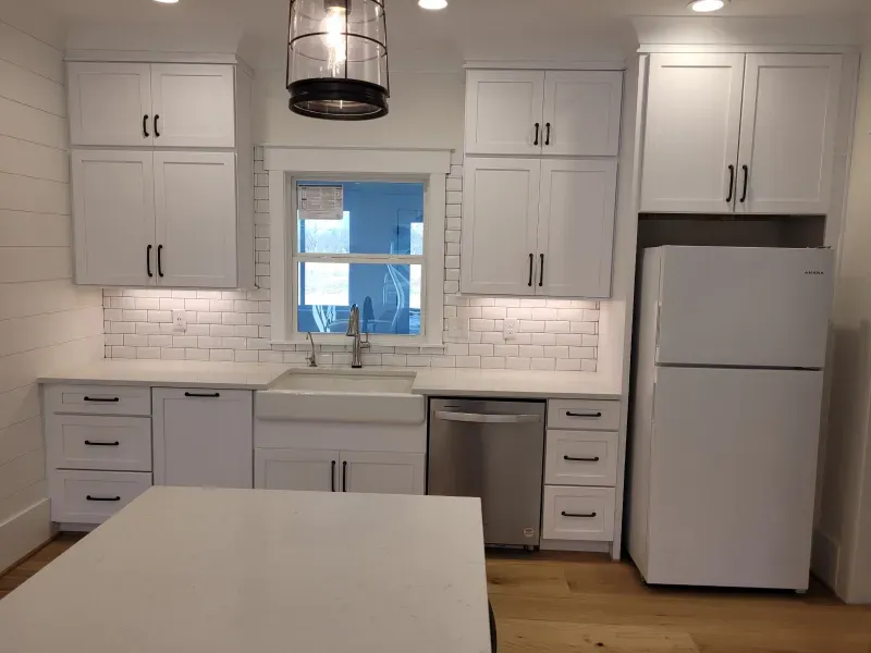 White kitchen with cabinets, sink, dishwasher, and refrigerator; a light fixture hangs overhead.