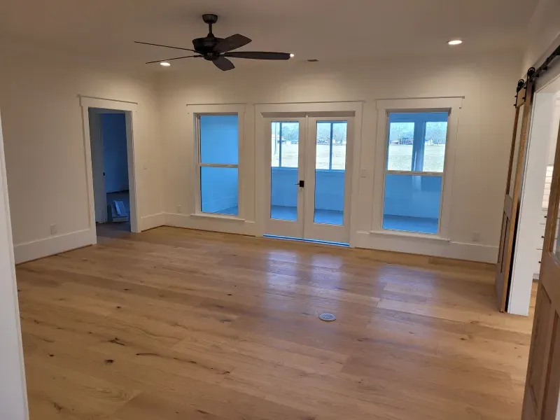 Empty room with wood floors, white walls, large windows, and a ceiling fan.
