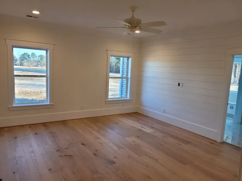 Empty bedroom with wood floors, white walls, two windows, and a ceiling fan.
