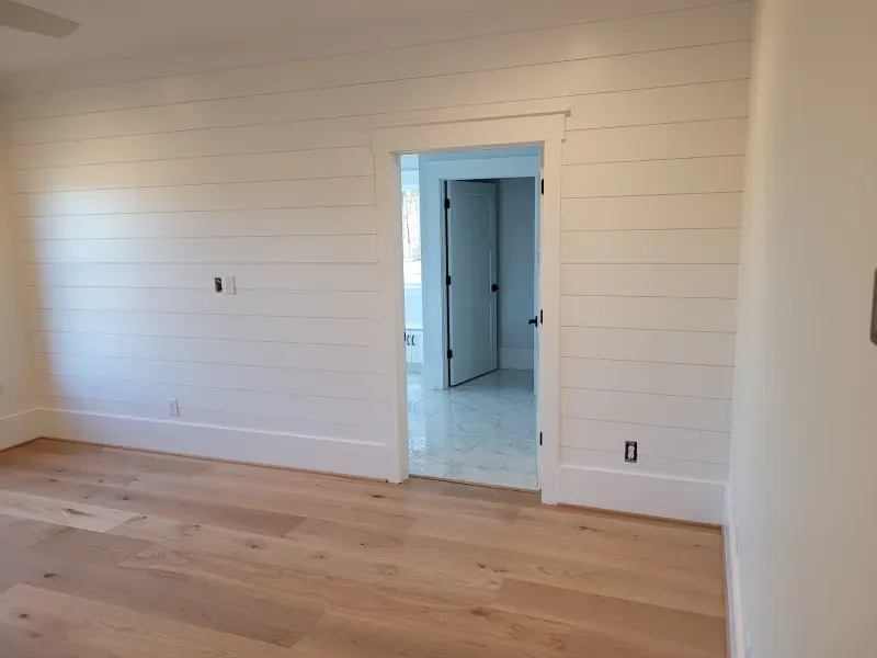 White-walled room with wood floor; a doorway leads to another room. One wall has horizontal planks.