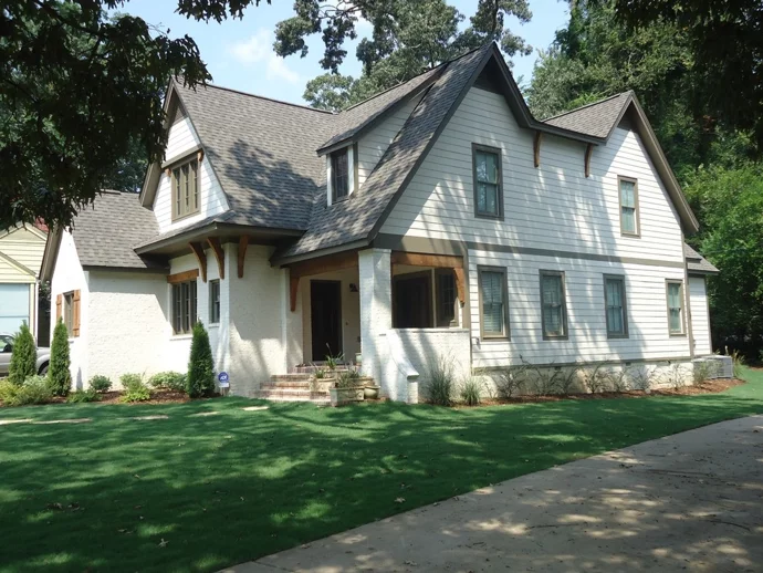 Two-story house with light siding, dark roof, and lush green lawn.