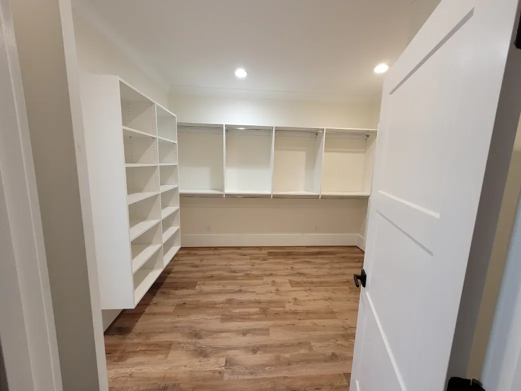 Empty white-shelved pantry with wood-look floor, viewed through an open white door.