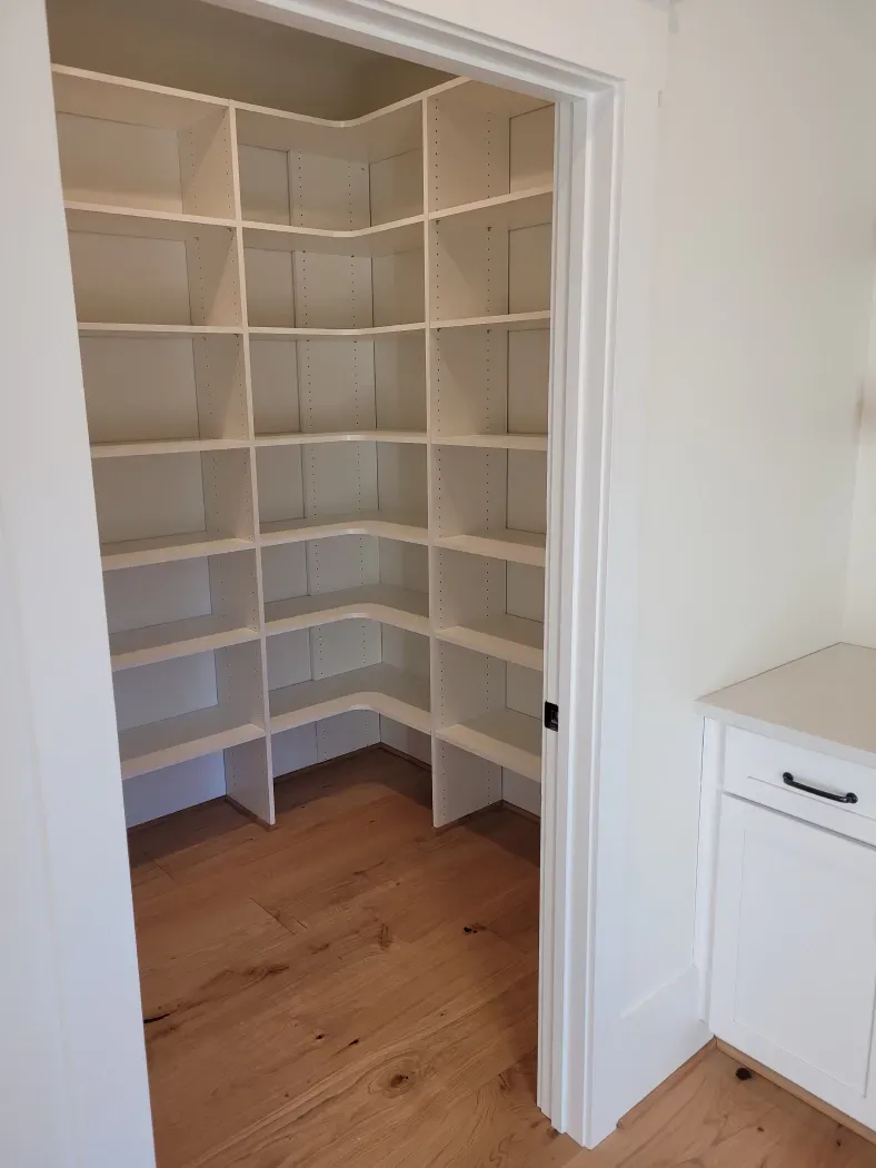 White pantry with shelves, hardwood floor, viewed through a doorway.