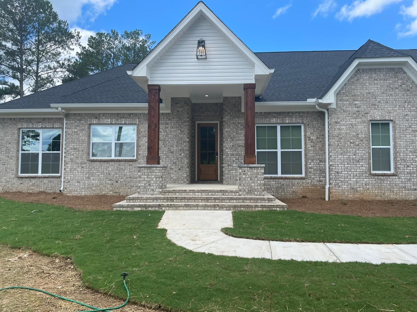 Brick home with white trim, brown door, and columns. Lush green lawn and sidewalk.