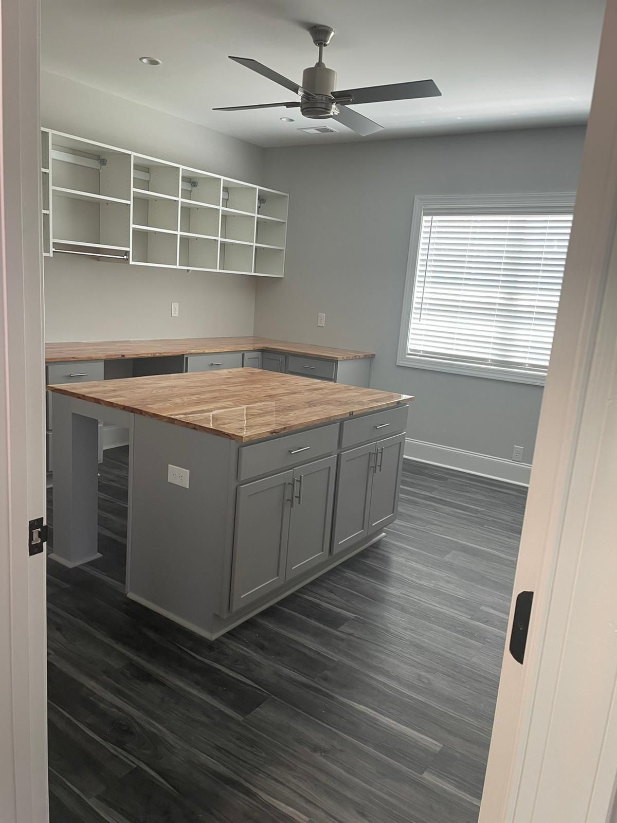Gray and white craft room with large island, cabinets, and workspace with dark wood floors.