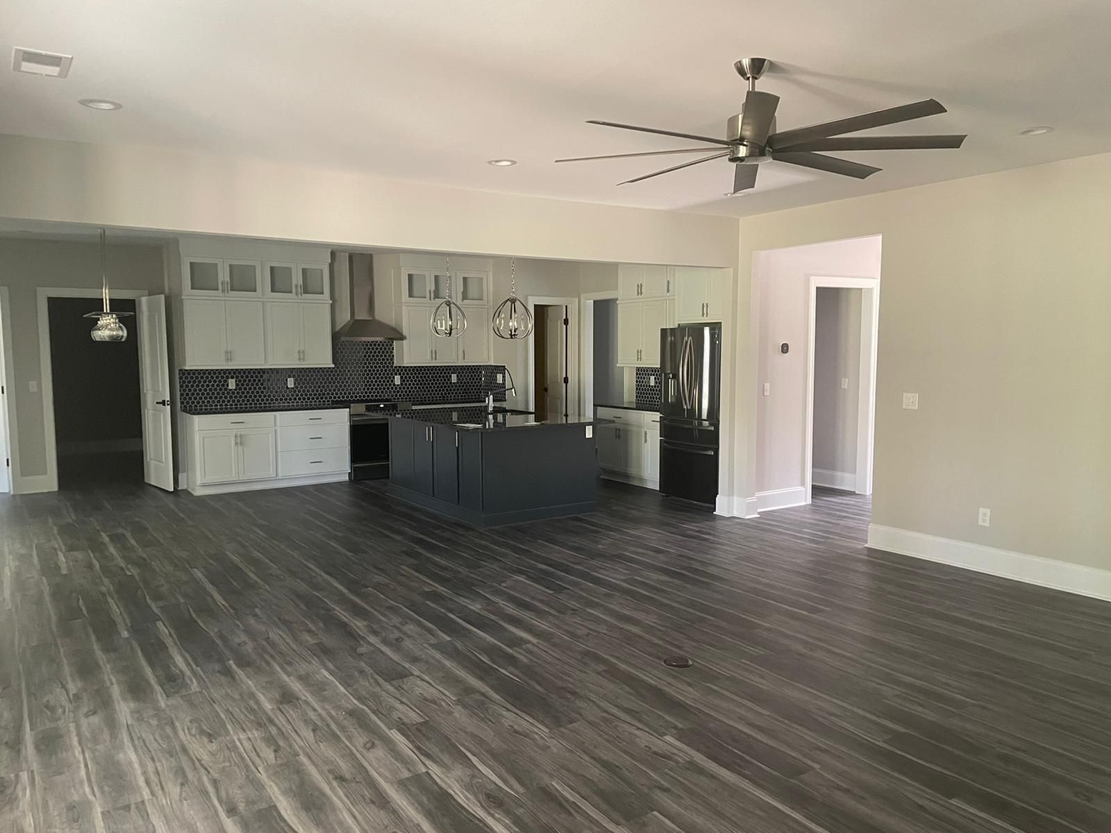 Open-concept kitchen with dark wood floors, light gray cabinets, and a dark island. A ceiling fan hangs above.