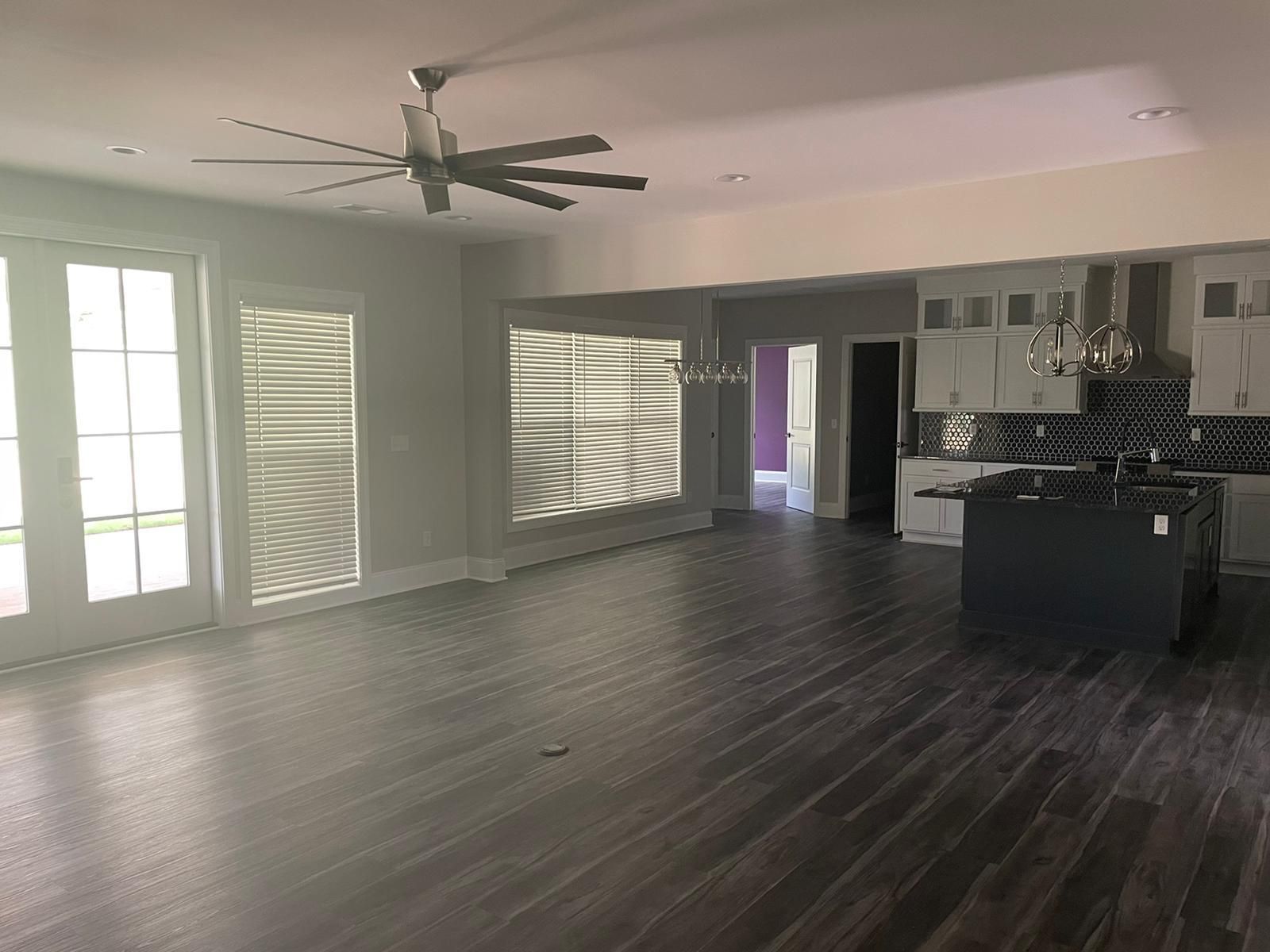Spacious, empty room with wood floors, large windows, and a kitchen area.