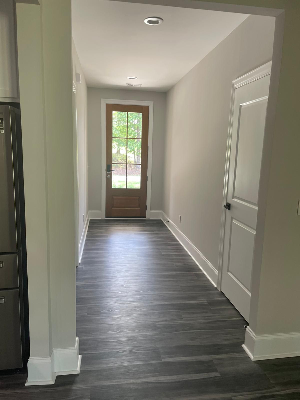 Hallway with dark floor, grey walls, white trim, and a wooden door at the end.