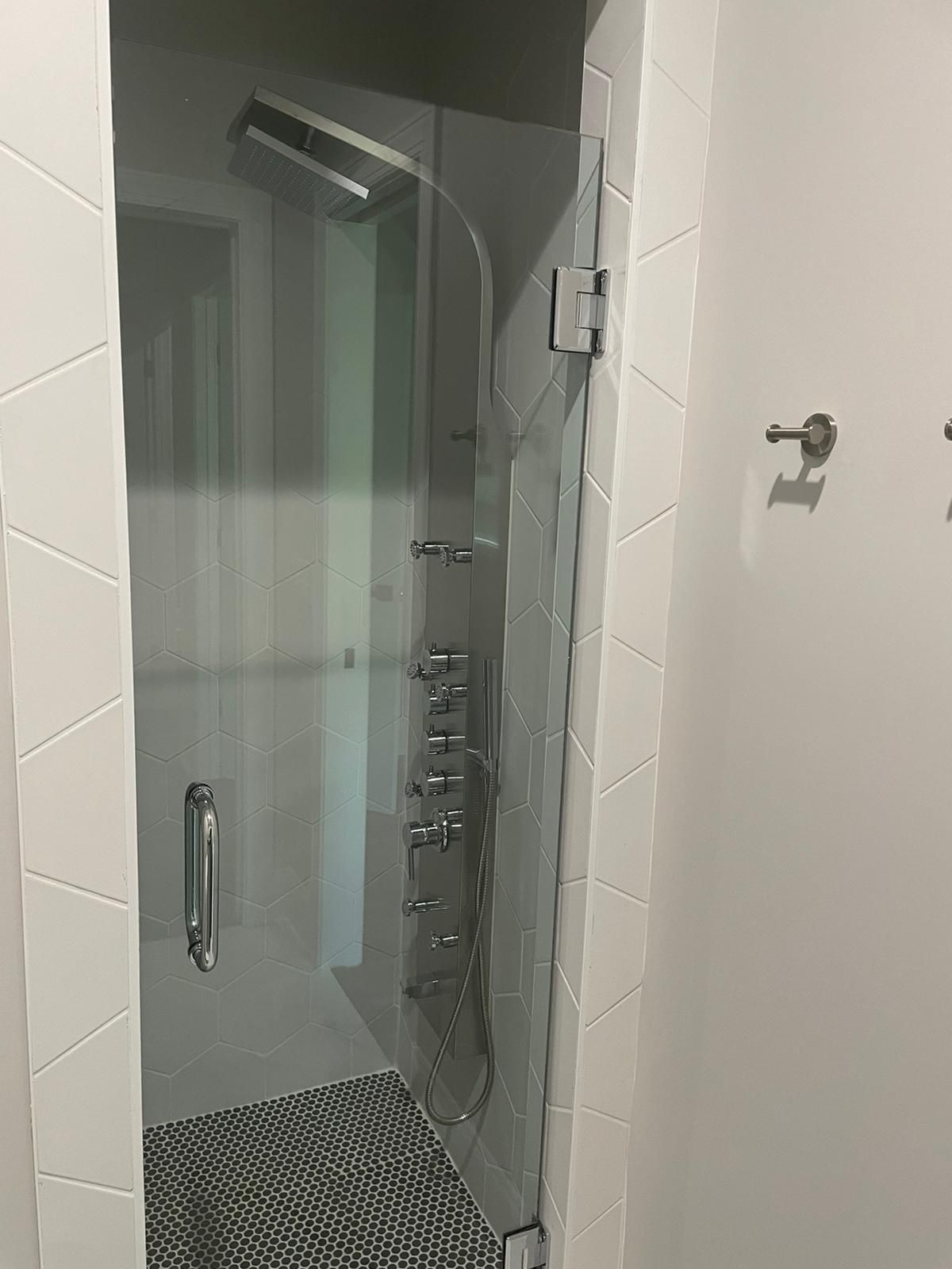 Glass shower door with silver shower fixtures and white and gray tile.