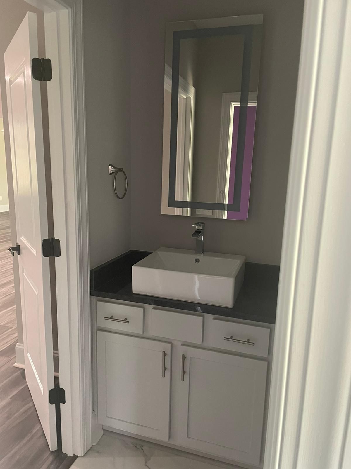 A small bathroom with a white sink and cabinet, silver-framed mirror, and gray walls.