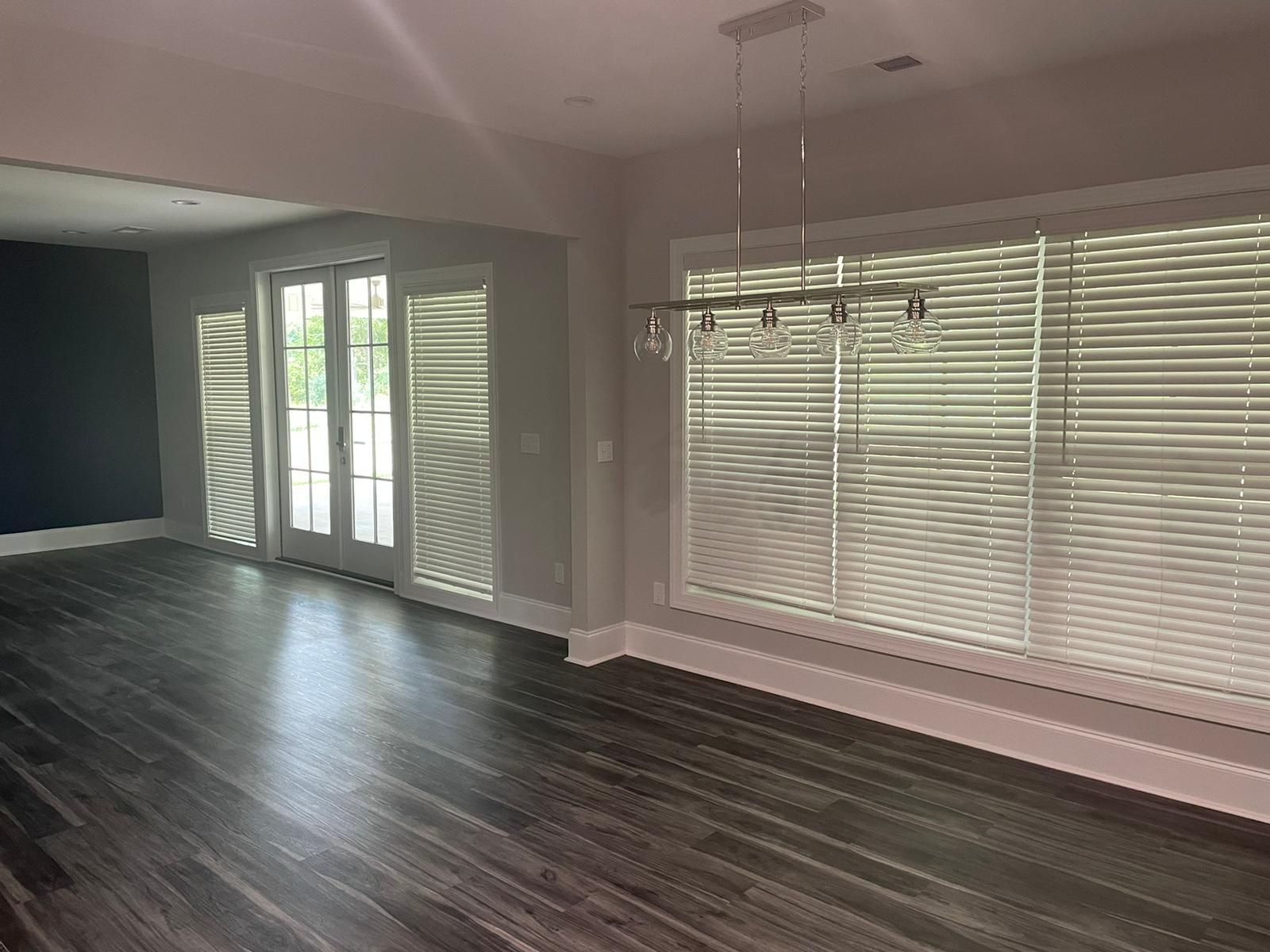 Empty dining room with dark wood floors, large windows, and a hanging chandelier.