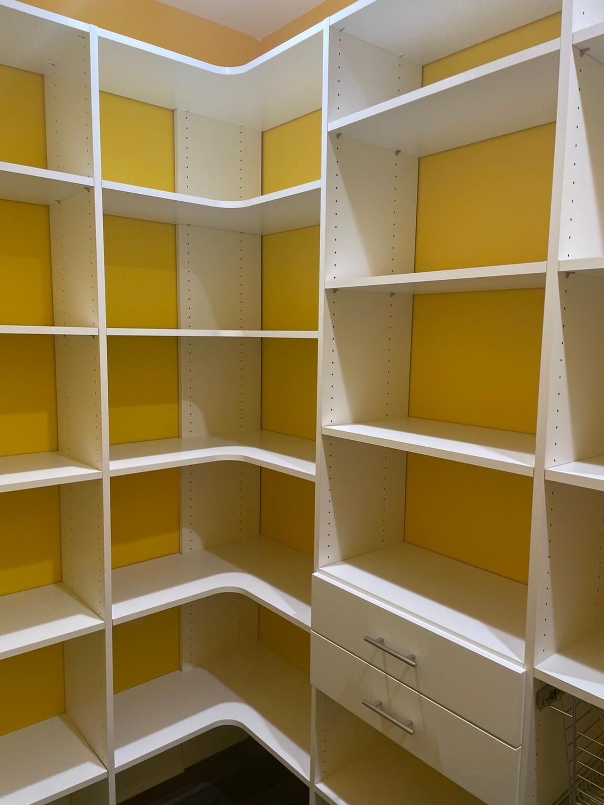 White built-in closet with yellow backing, corner design, shelves, and drawers.