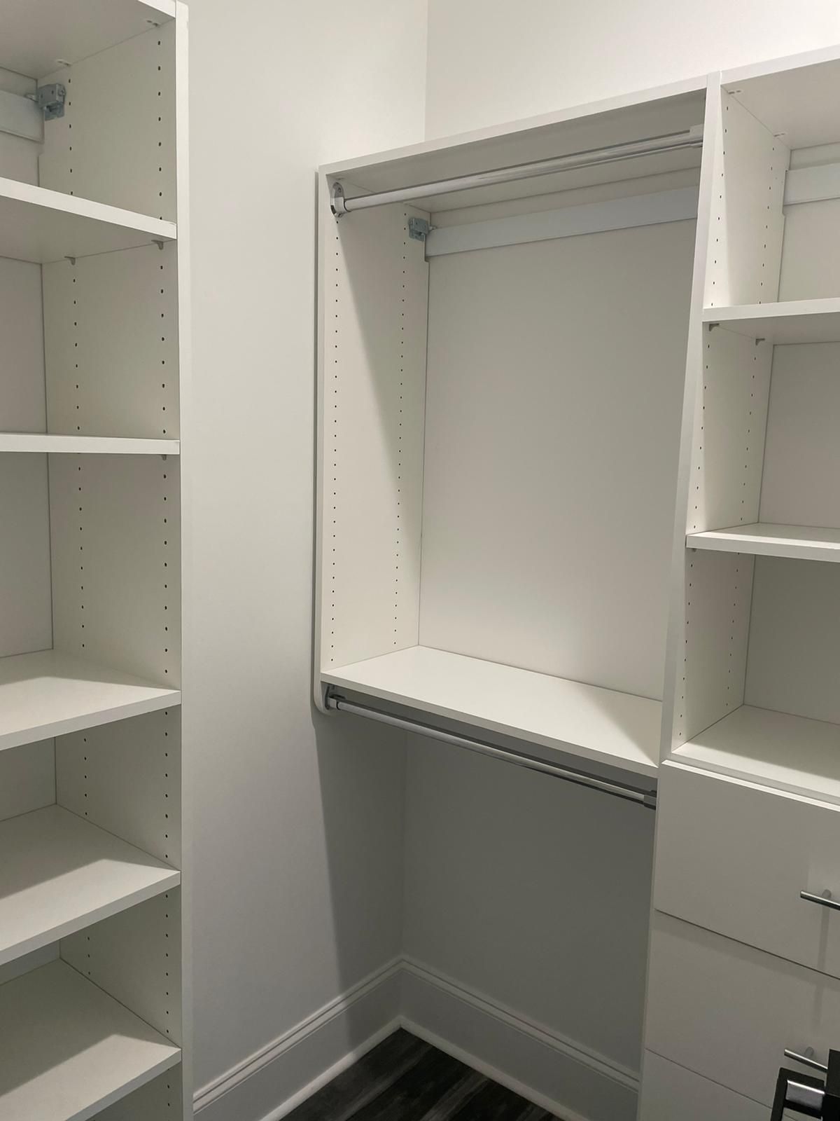 Empty white closet with shelves, hanging rod, and drawers in a corner.