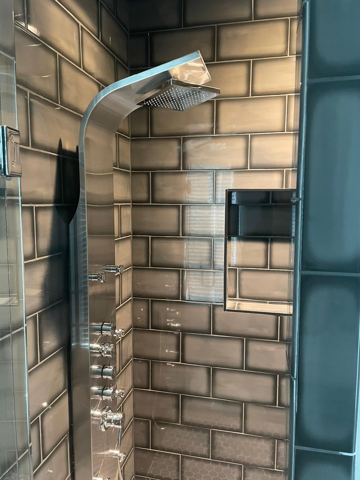 Shower with silver fixtures and a built-in shelf, set against gray brick tile walls.