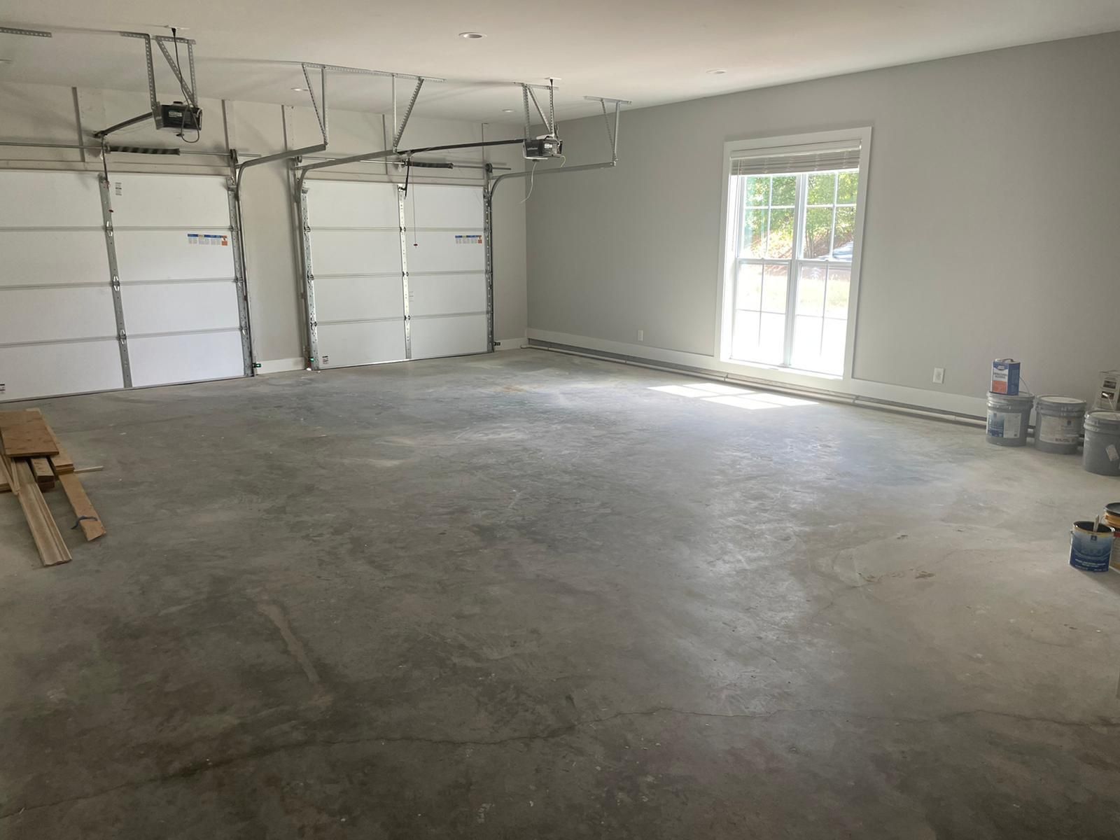 Empty garage with concrete floor, three garage doors, a window, and paint supplies.