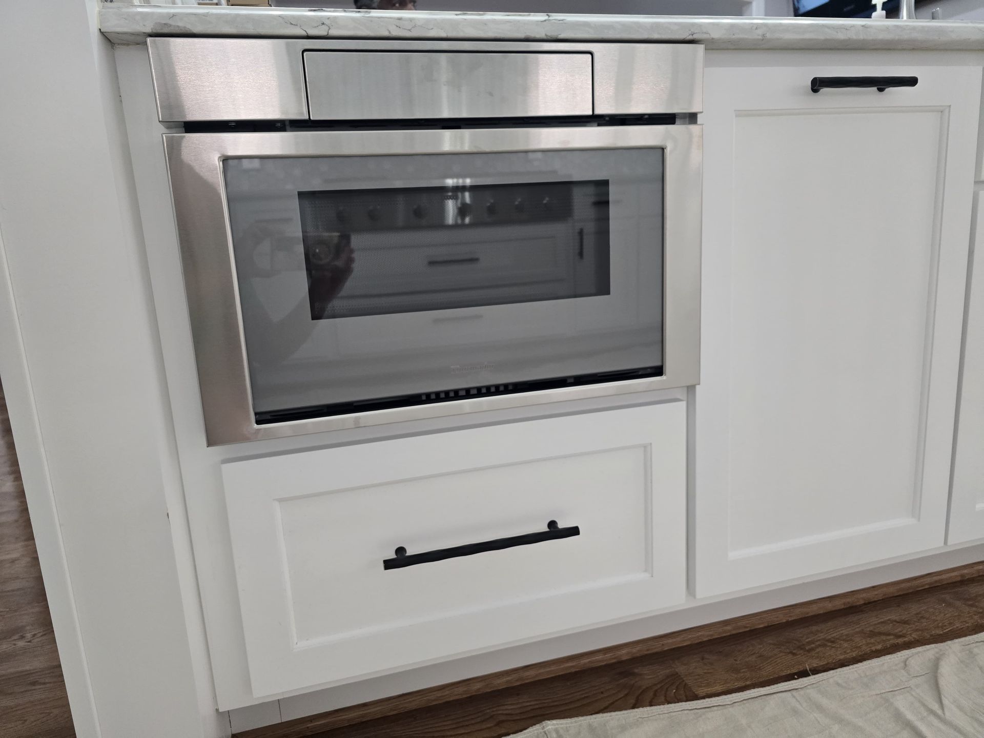 Built-in stainless steel microwave oven above a drawer, mounted in white kitchen cabinetry.