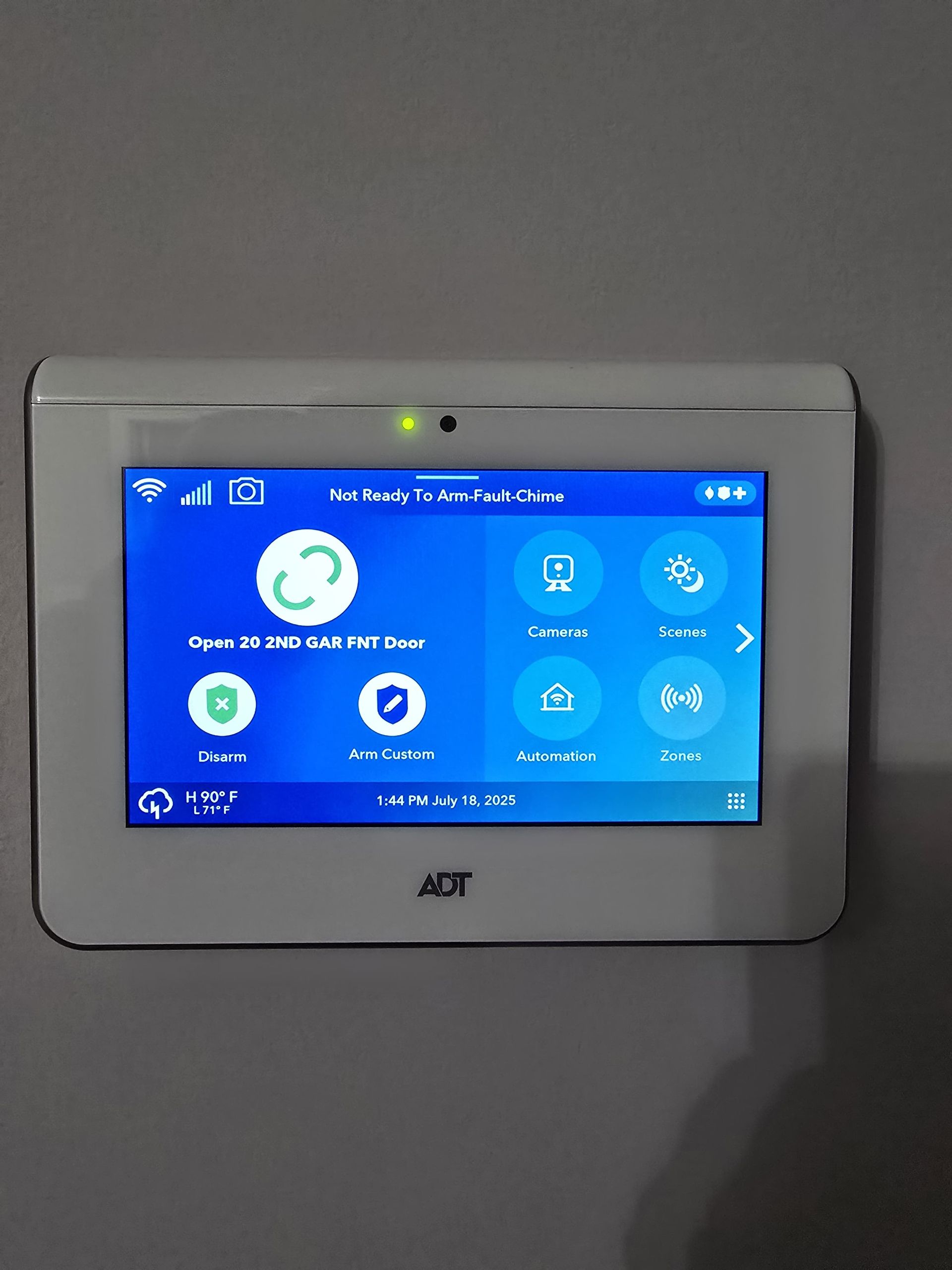 ADT home security system control panel on a wall, showing app icons on a blue screen.