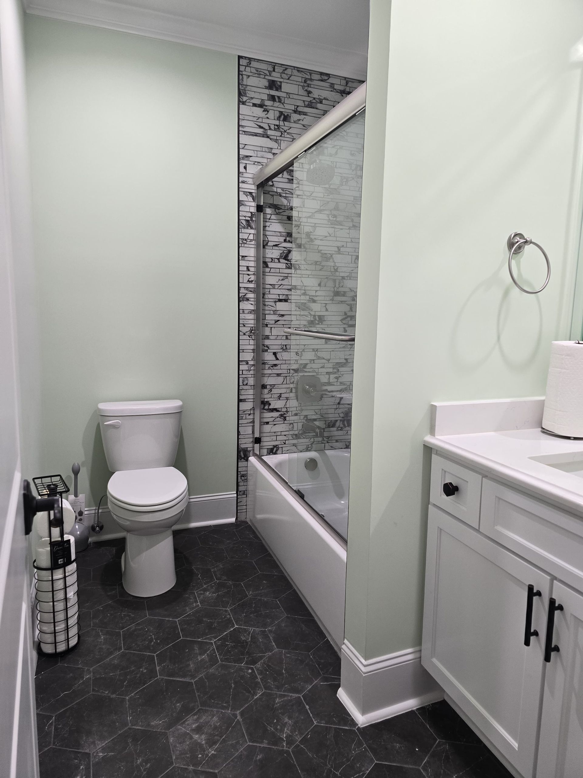 Bathroom with a toilet, vanity, bathtub/shower, and dark gray floor; walls are light green.