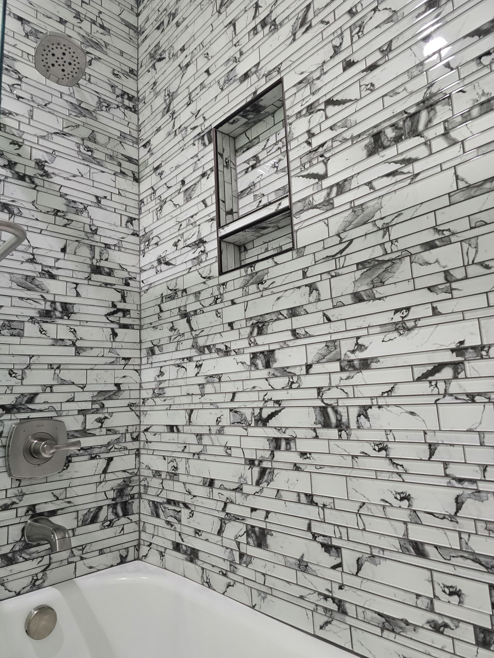Shower with white and black textured tile, a built-in shelf, and silver fixtures.