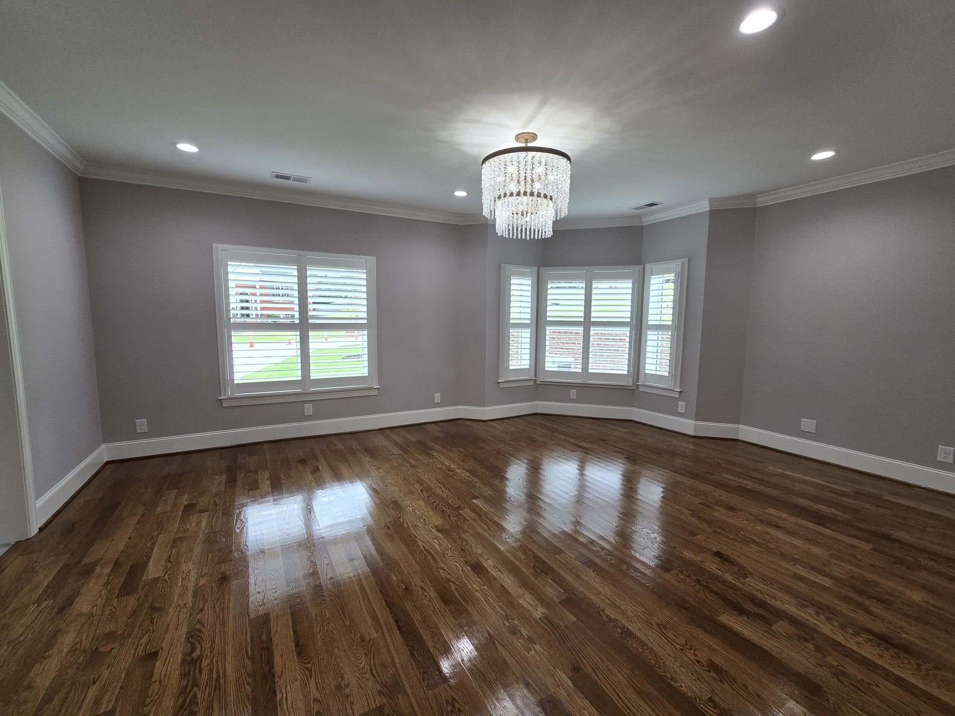 Empty room with hardwood floors, gray walls, white trim, and a chandelier.