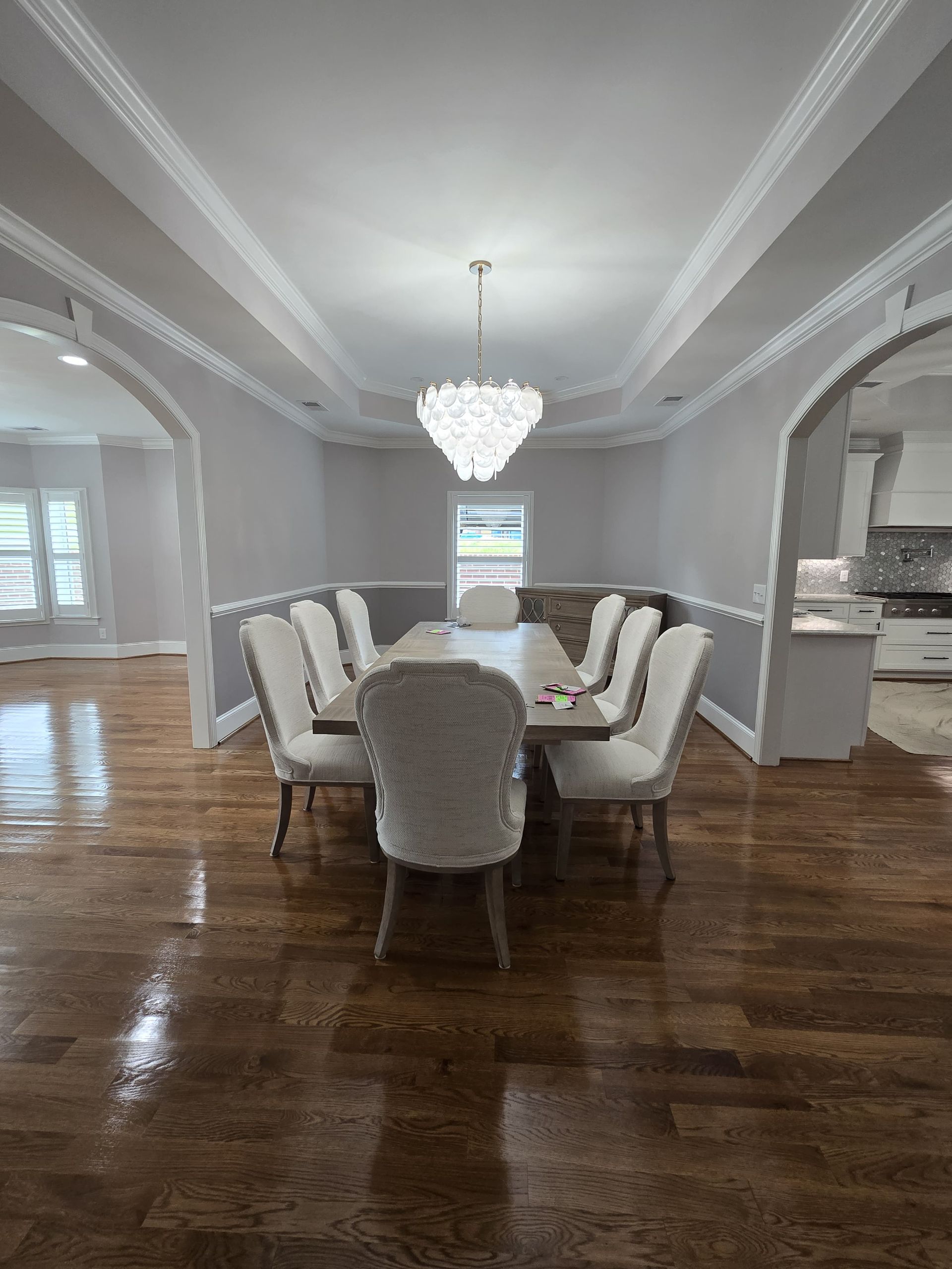 Formal dining room with a chandelier above a table surrounded by white chairs. Hardwood floors.
