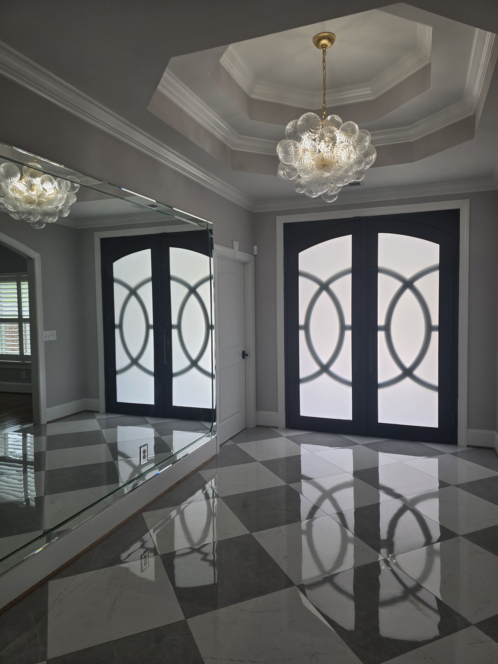 Elegant room with black doors, a large mirror, and a chandelier. Checkerboard floor.