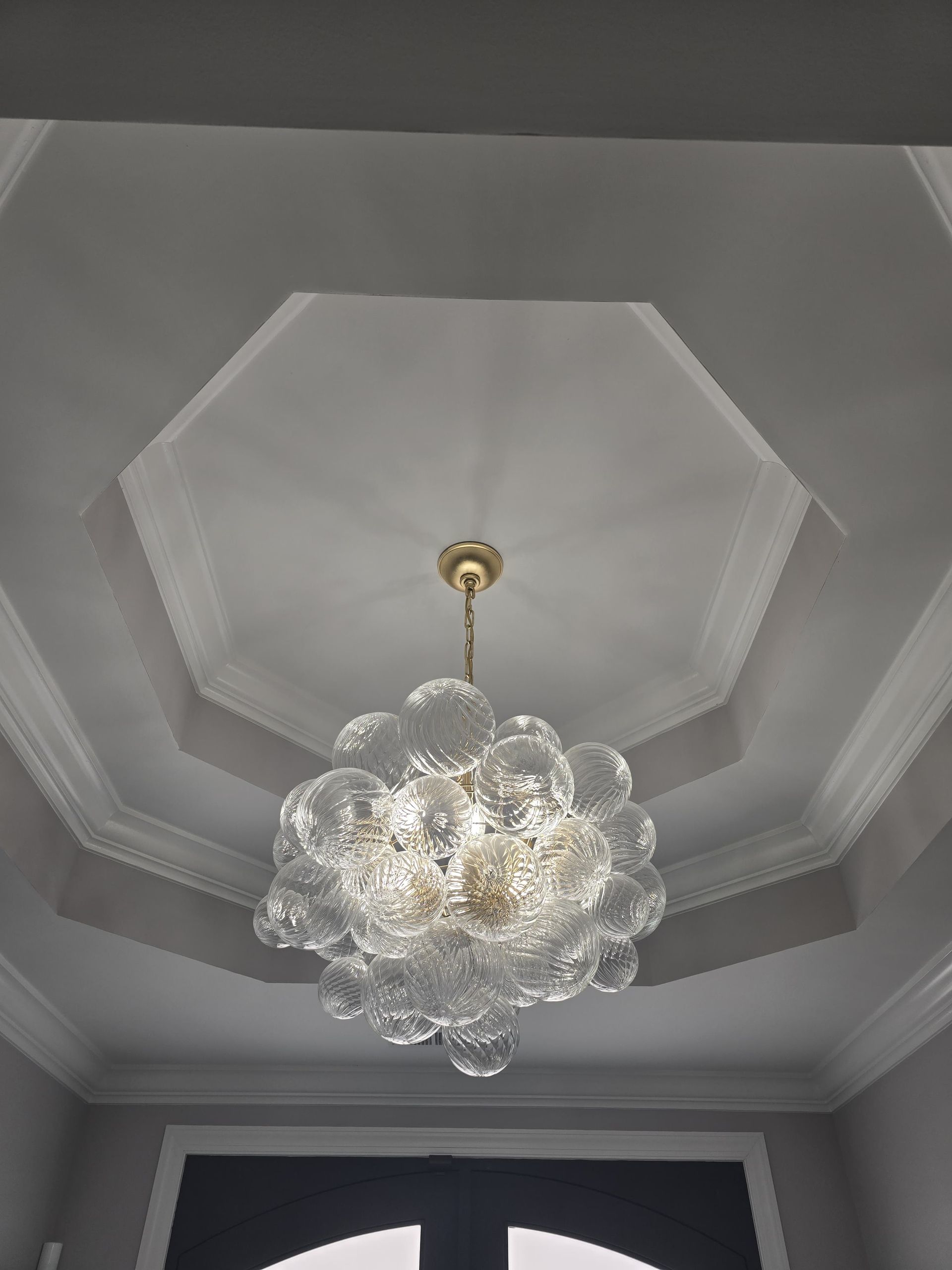 Chandelier hangs from a decorative ceiling, in a gray and white room.