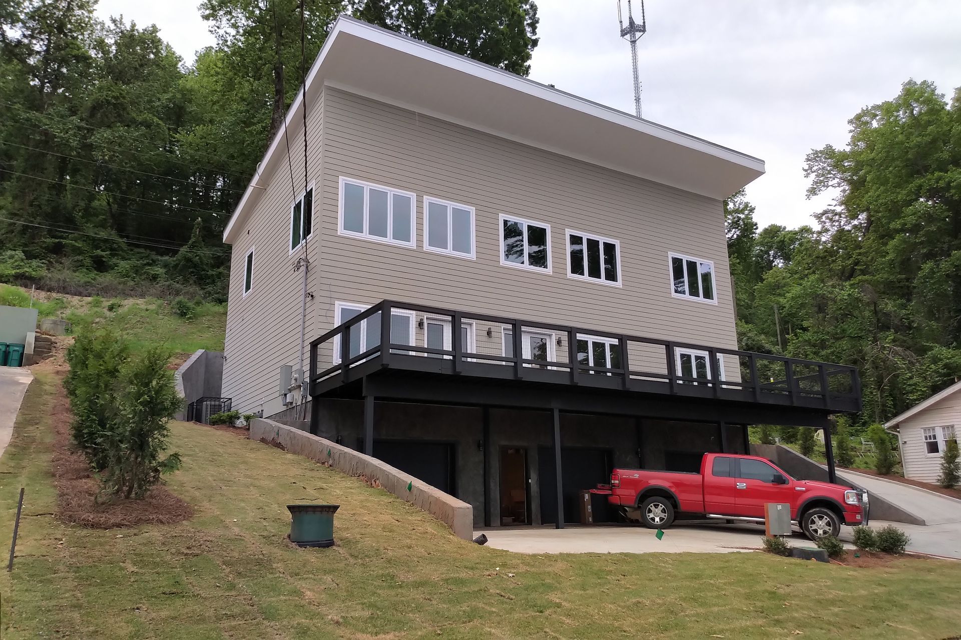 A three-story tan house with a red truck parked in front. Black deck and garage. Hillside setting.