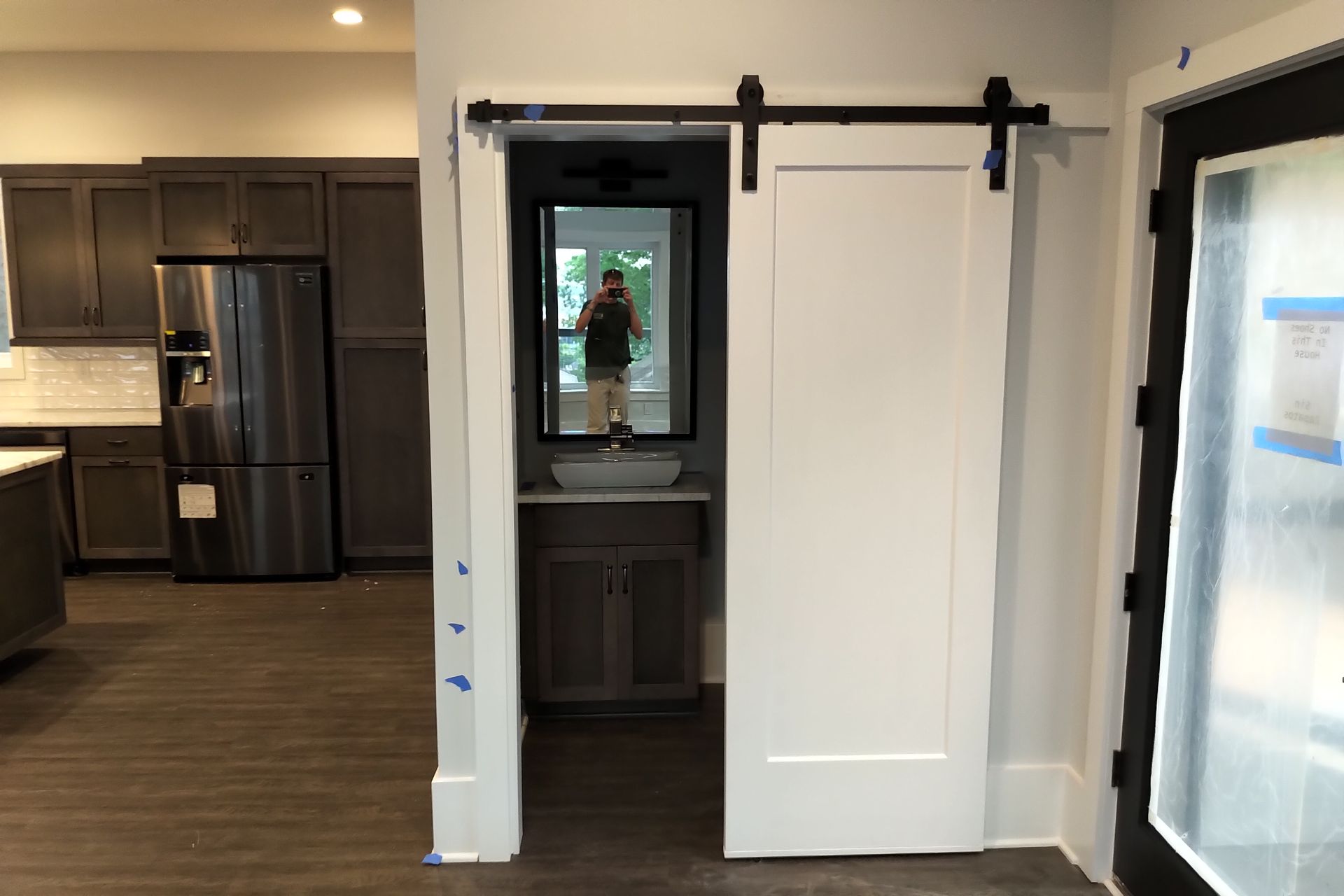 Barn door in an entrance to a powder room, showing a sink and mirror. Brown cabinets, gray and white walls.