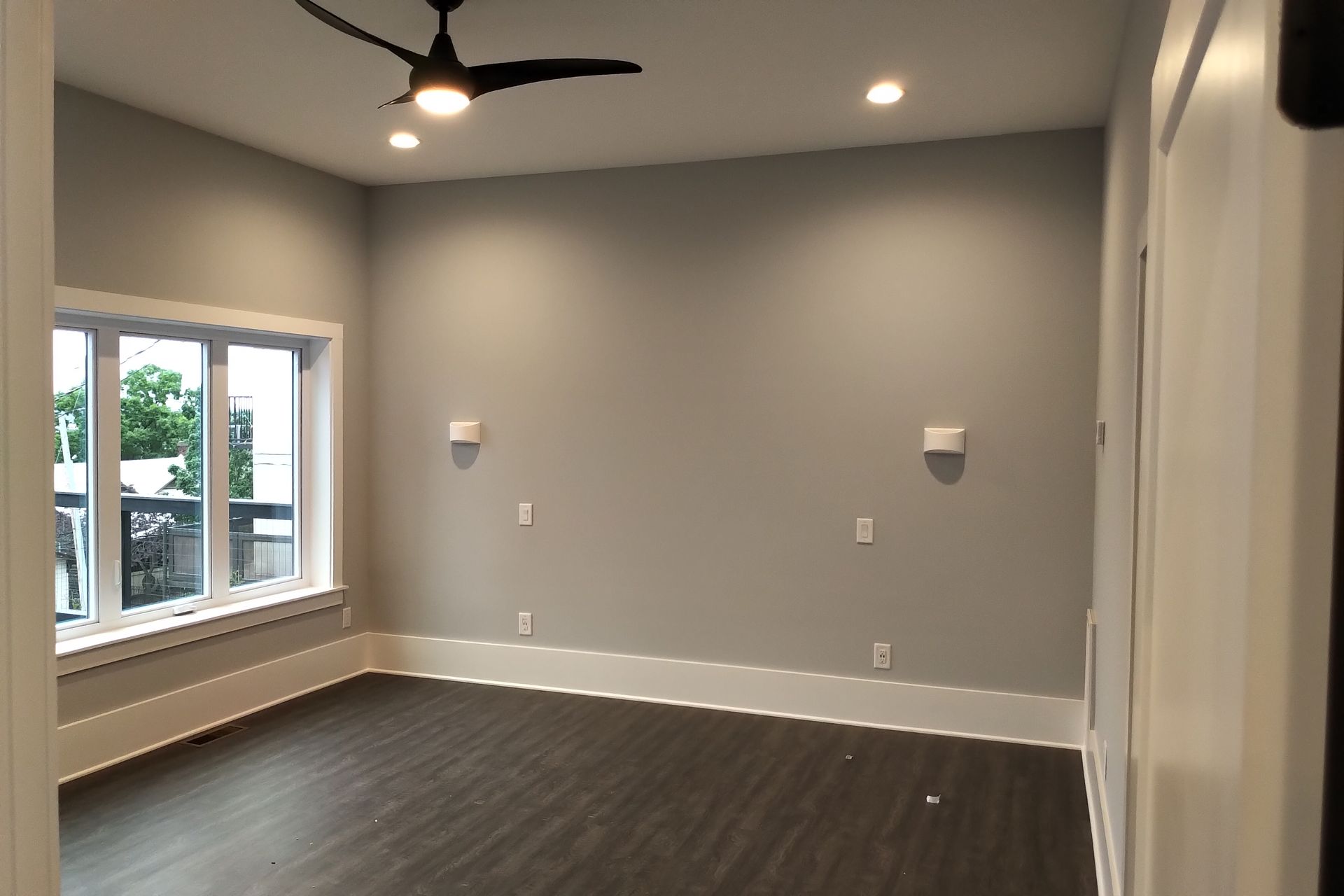Empty room with gray walls, dark floor, white trim, and a window.
