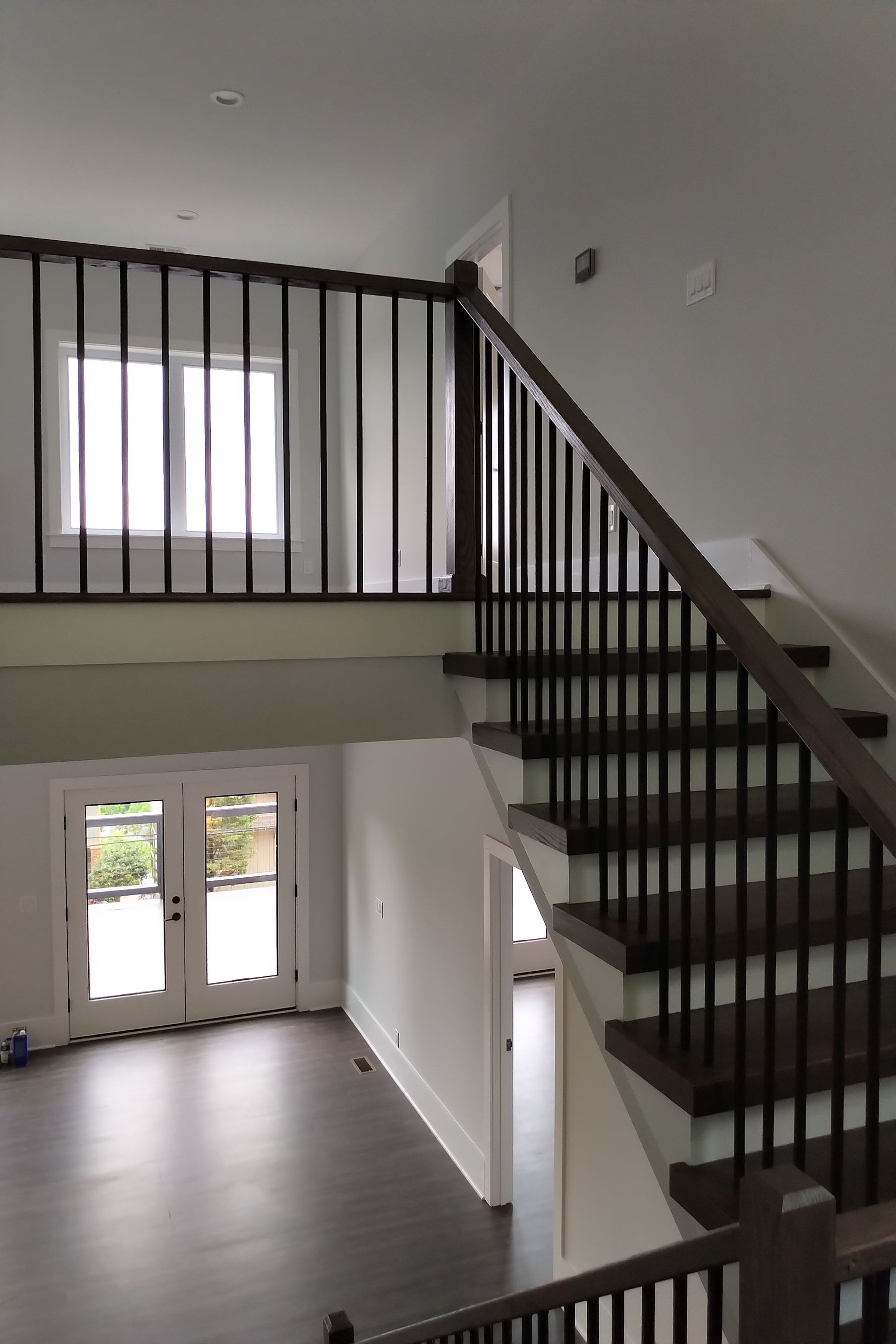 Interior view of a home with a staircase. Brown railing and stairs with dark hardwood floors. Light gray walls.